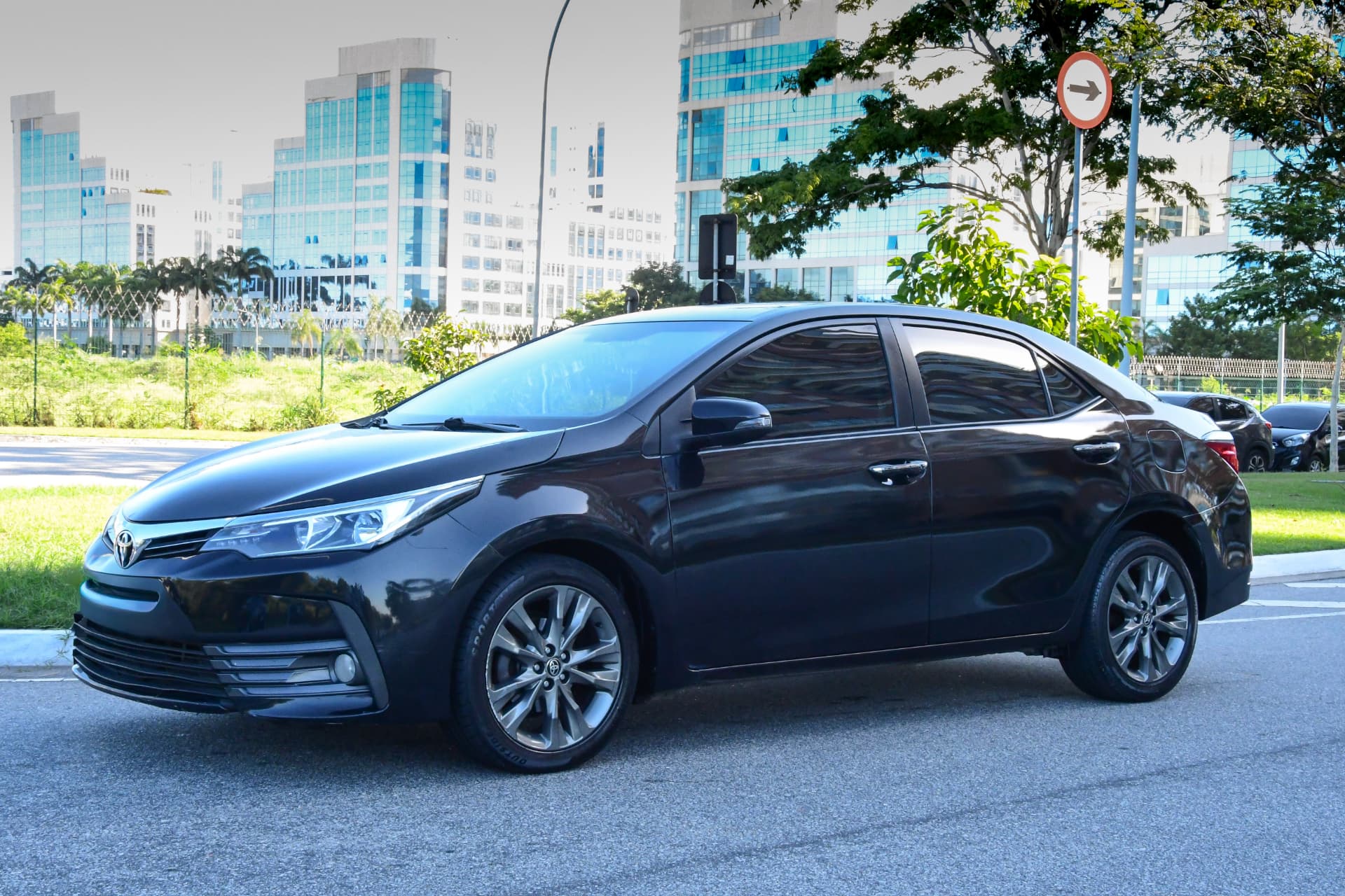 Sedã escuro estacionado em via urbana com prédios ao fundo